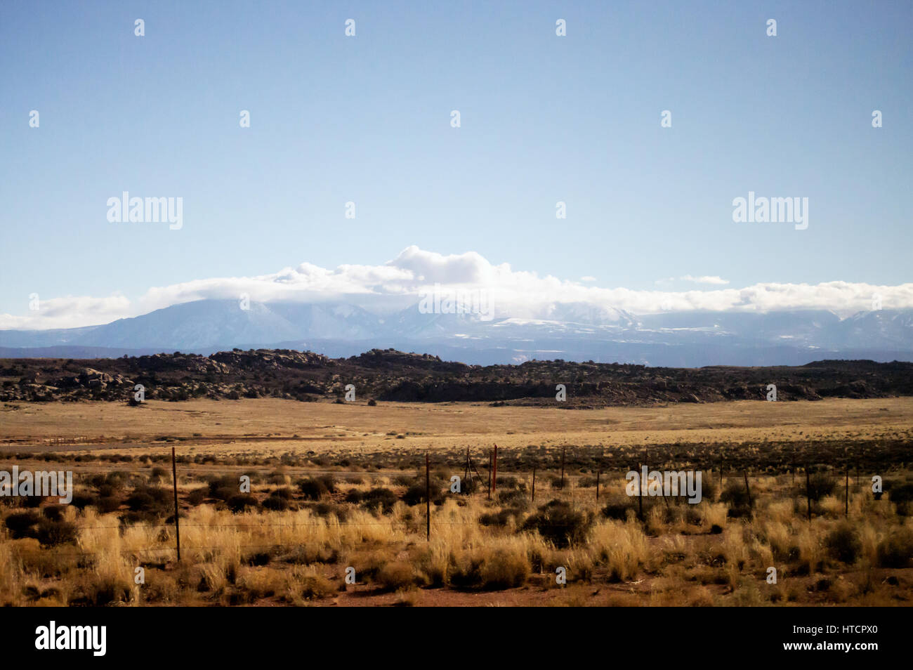A desert landscape with a an old fence and scrub brush with mountain peaks behind it. Stock Photo