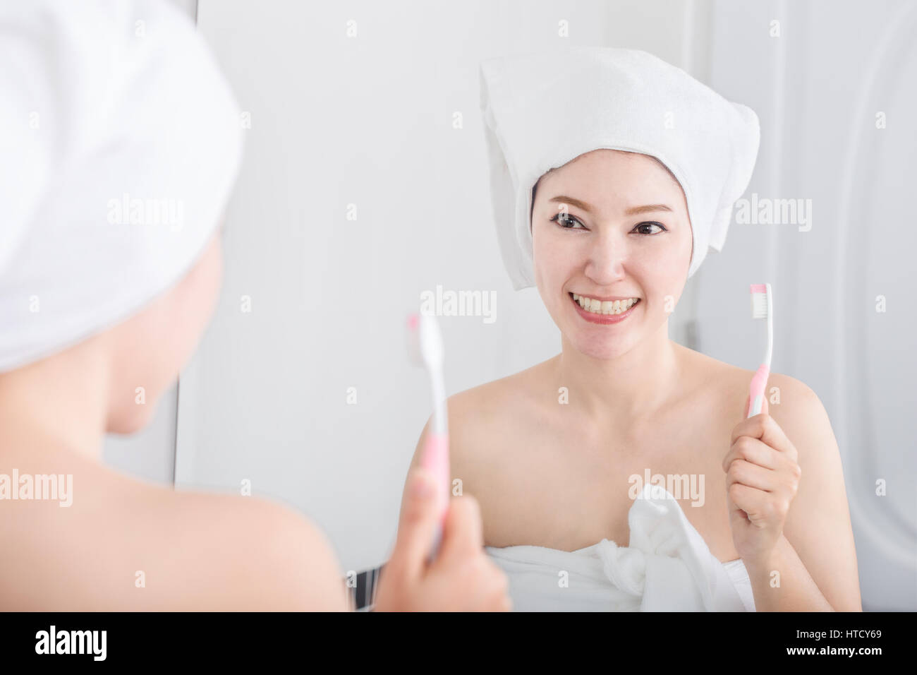 woman in bath towel brushing teeth with mirror in the bathroom Stock