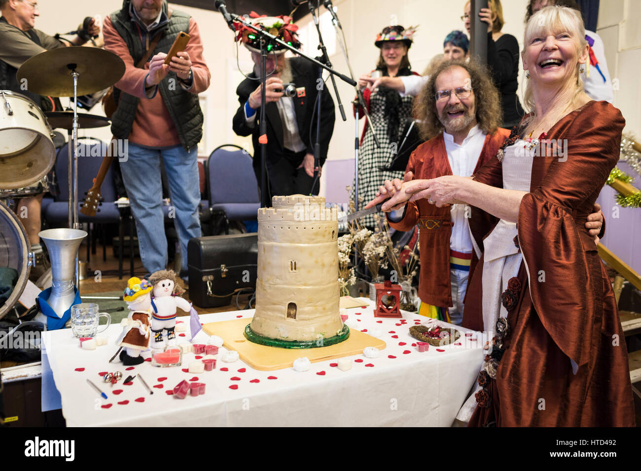 Newly-wed Morris dancing couple cutting the cake at their wedding reception (cake inspired by the great keep of Pembroke castle in Wales). Stock Photo