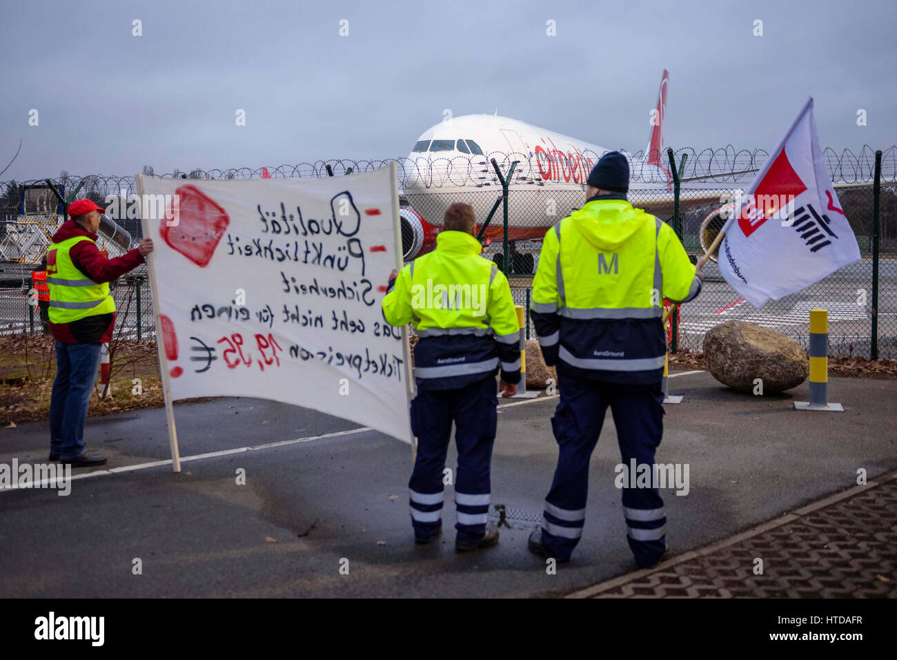 Ground staff hold up flags and a banner near the runway at Tegel Airport in Berlin, Germany, 10 March 2017. German trade union Verdi had called on some 2,000 ground staff to join the strike. The strike began on 10 March 2017 at 03:00 GMT and is to end on 11 March 2017 at 04:00 GMT. The main reason for the strike is the ongoing labour dispute between Verdi and the Forum of Ground Transport Service Providers in which the companies operating at the airports are organized. The trade union is demanding a pay rise for ground staff. Photo: Gregor Fischer/dpa Stock Photo