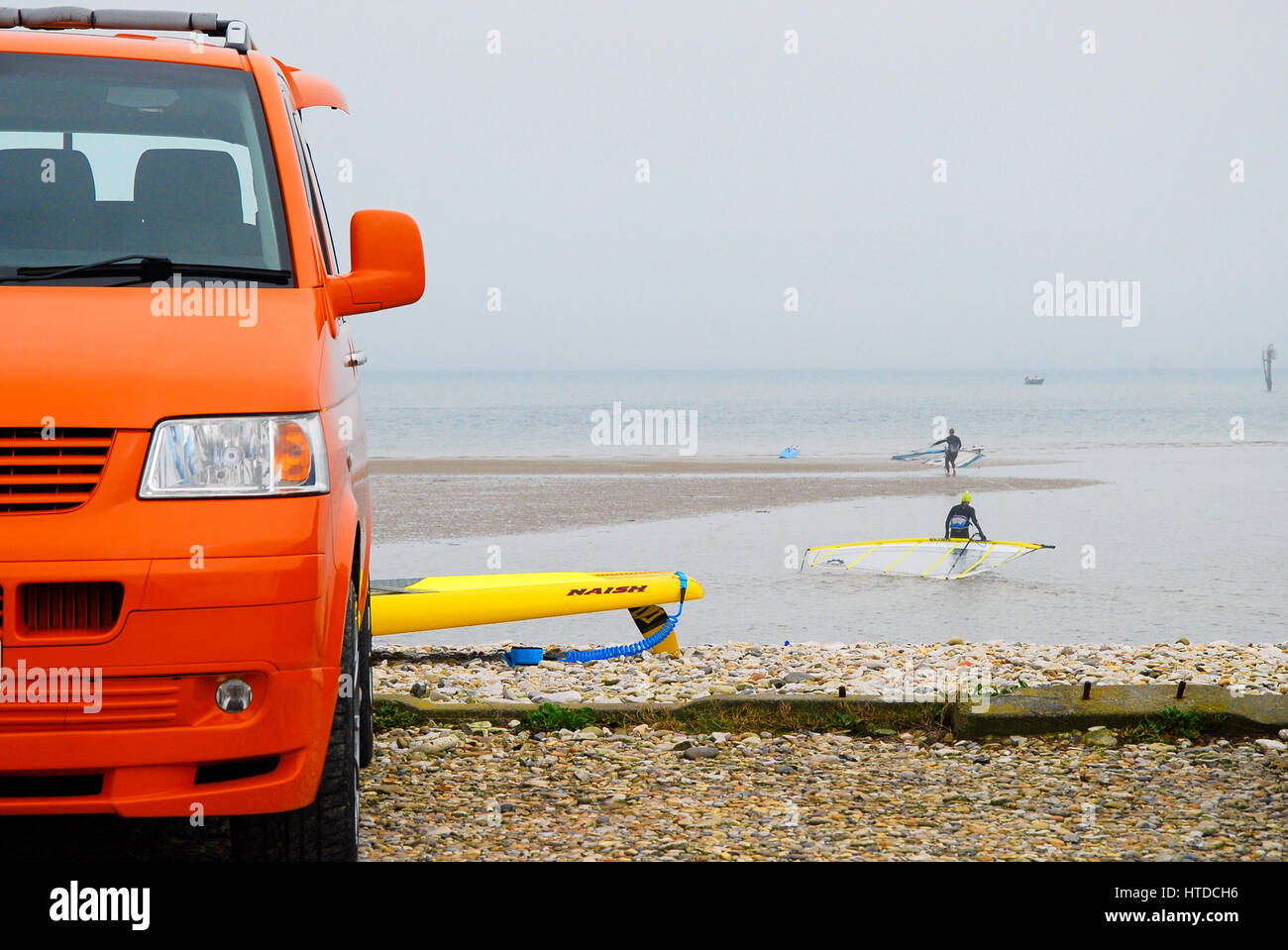 Weymouth & Portland, Dorset, 2017, VW campervan owners enjoy Portland harbour on an overcast day. Their bright-orange VW van brightens up the dull day and gives the scene a 'California surfer' look. Stock Photo
