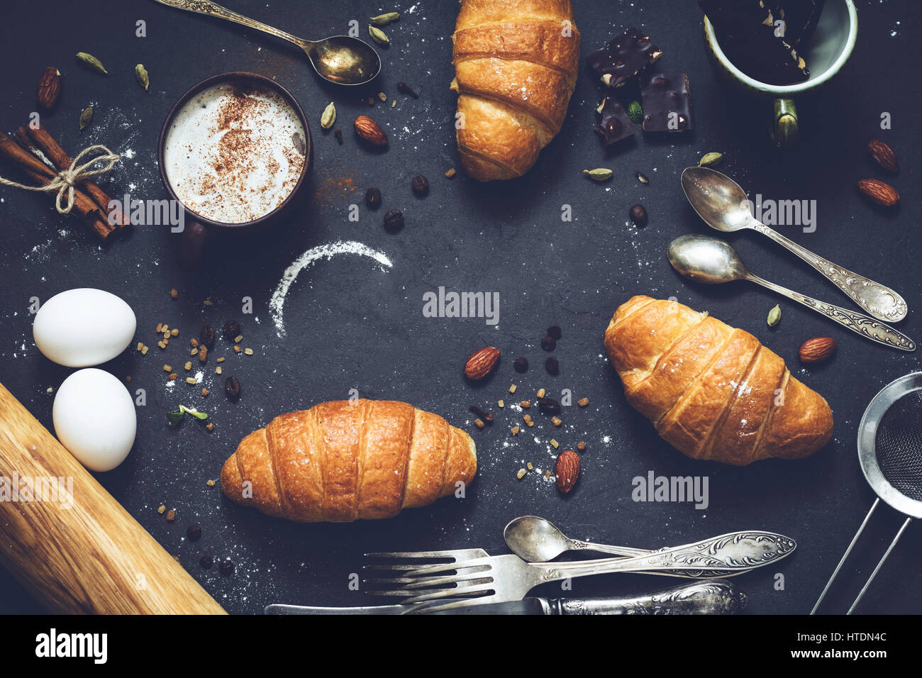 Coffee, croissants, chocolate, spices, nuts and vintage cutlery. Flat lay composition of sweet breakfast food on dark stone background with copy space Stock Photo