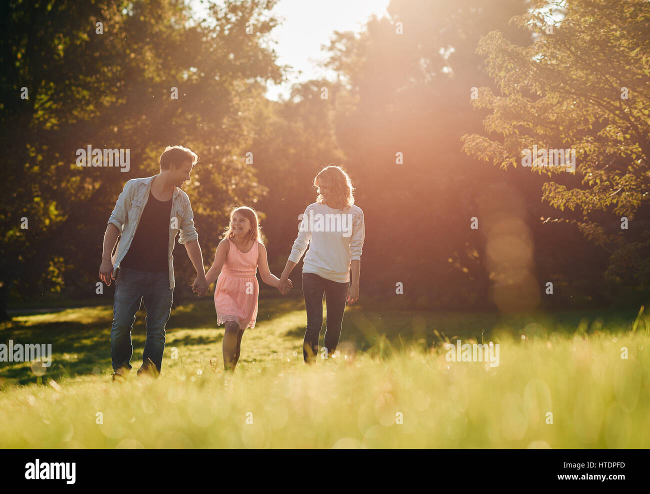 Smiling mother and father walking hand in hand with their little daughter in a park on a sunny summer afternoon Stock Photo