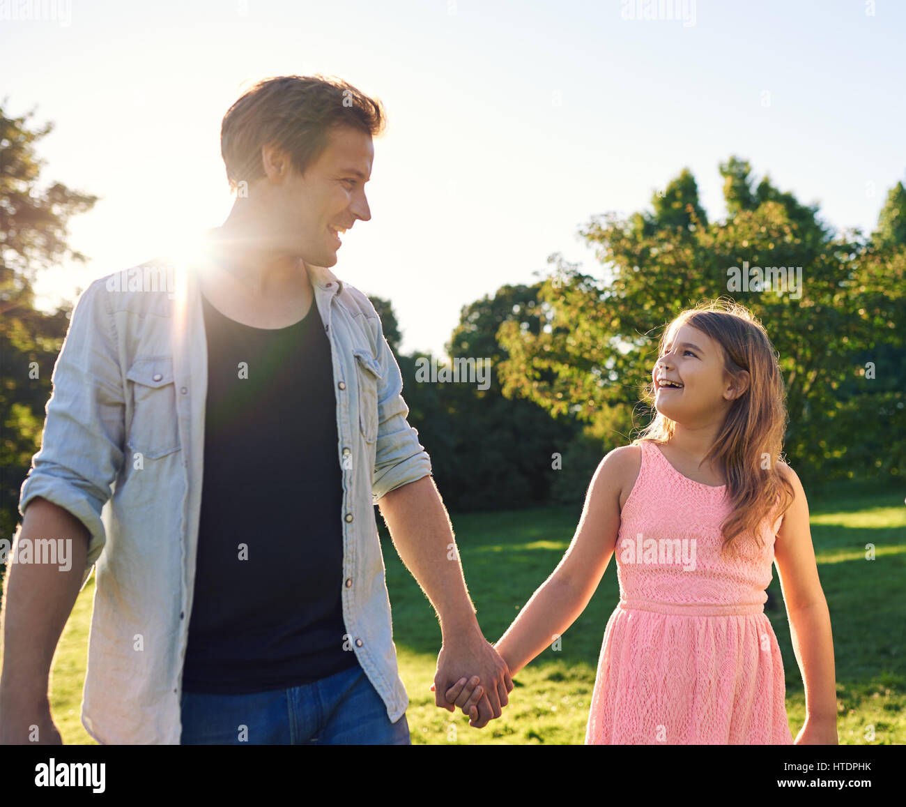 Proud father walking hand in hand with his smiling daughter while ...