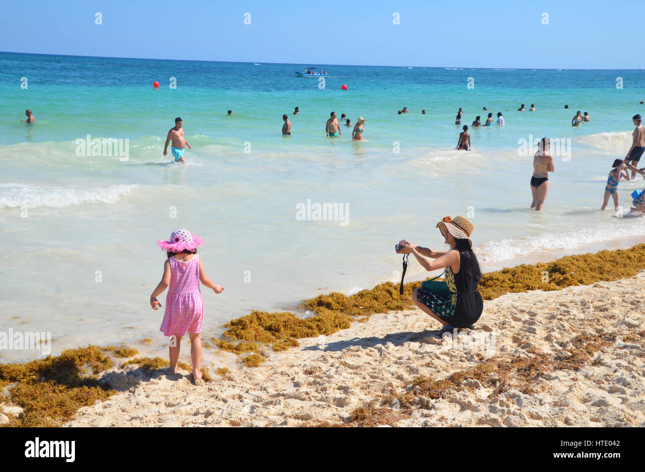 japanese tourist in sunhat takes photo of daughter in pink dress and hat on tulum beach Stock Photo