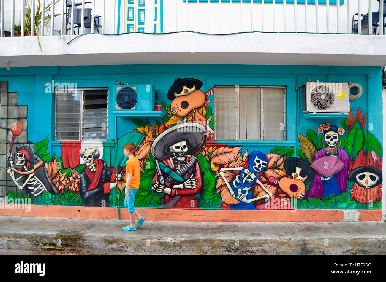 tourist boy walks in front of mexican mural street art on isla mujeres mexico Stock Photo