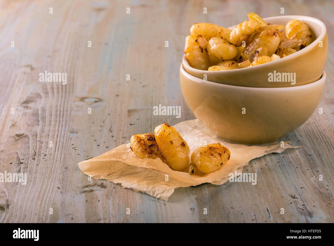 Horizontal photo of boiled and fried gnocchi on piece of paper in front of two bowls with single portion. Several pieces are served together with roas Stock Photo