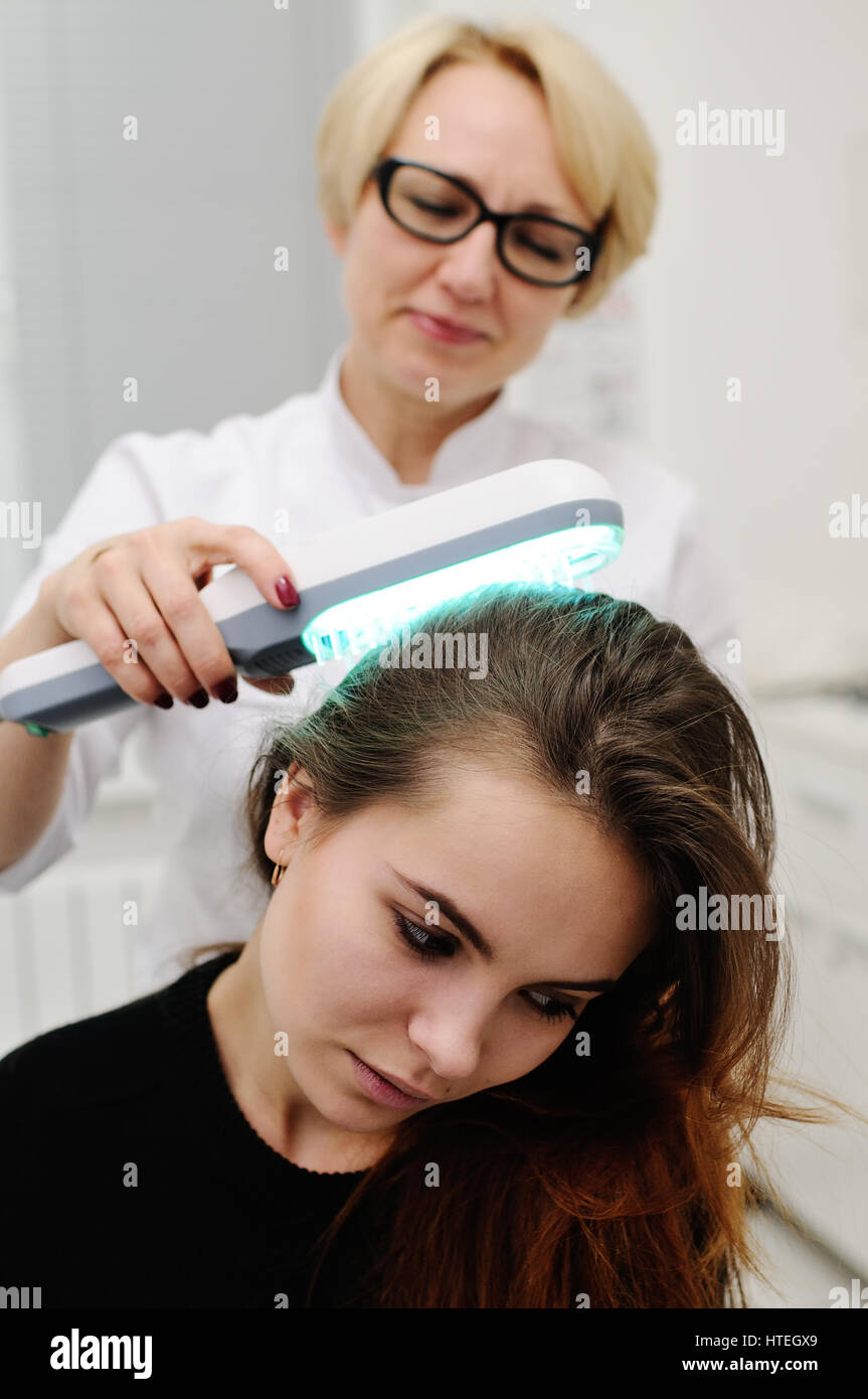 Doctor examines scalp a pretty young girl with special instrument UV lamp. Skin problems, dermatology, shingles, psoriasis, redness, prevention Stock Photo