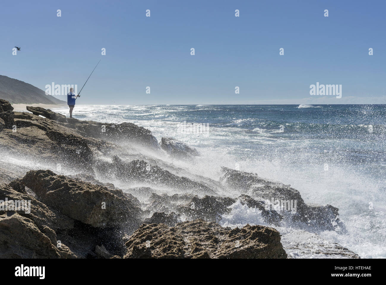 Angler standing on rocky coast with strong surf, iSimangaliso Wetland Park, KwaZulu-Natal, South Africa Stock Photo