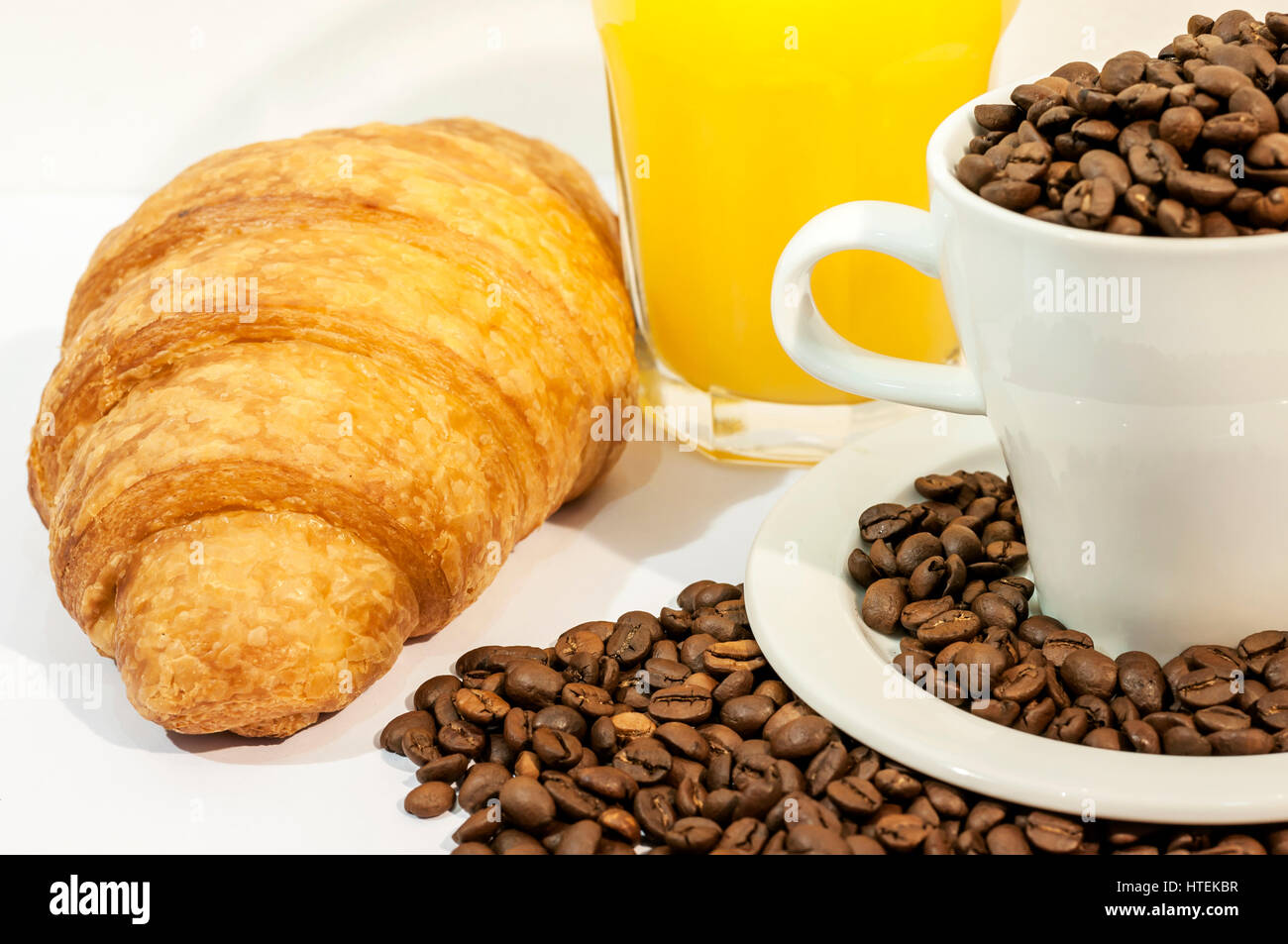 Cup of coffee filed with coffee beans with croissants, orange juice on