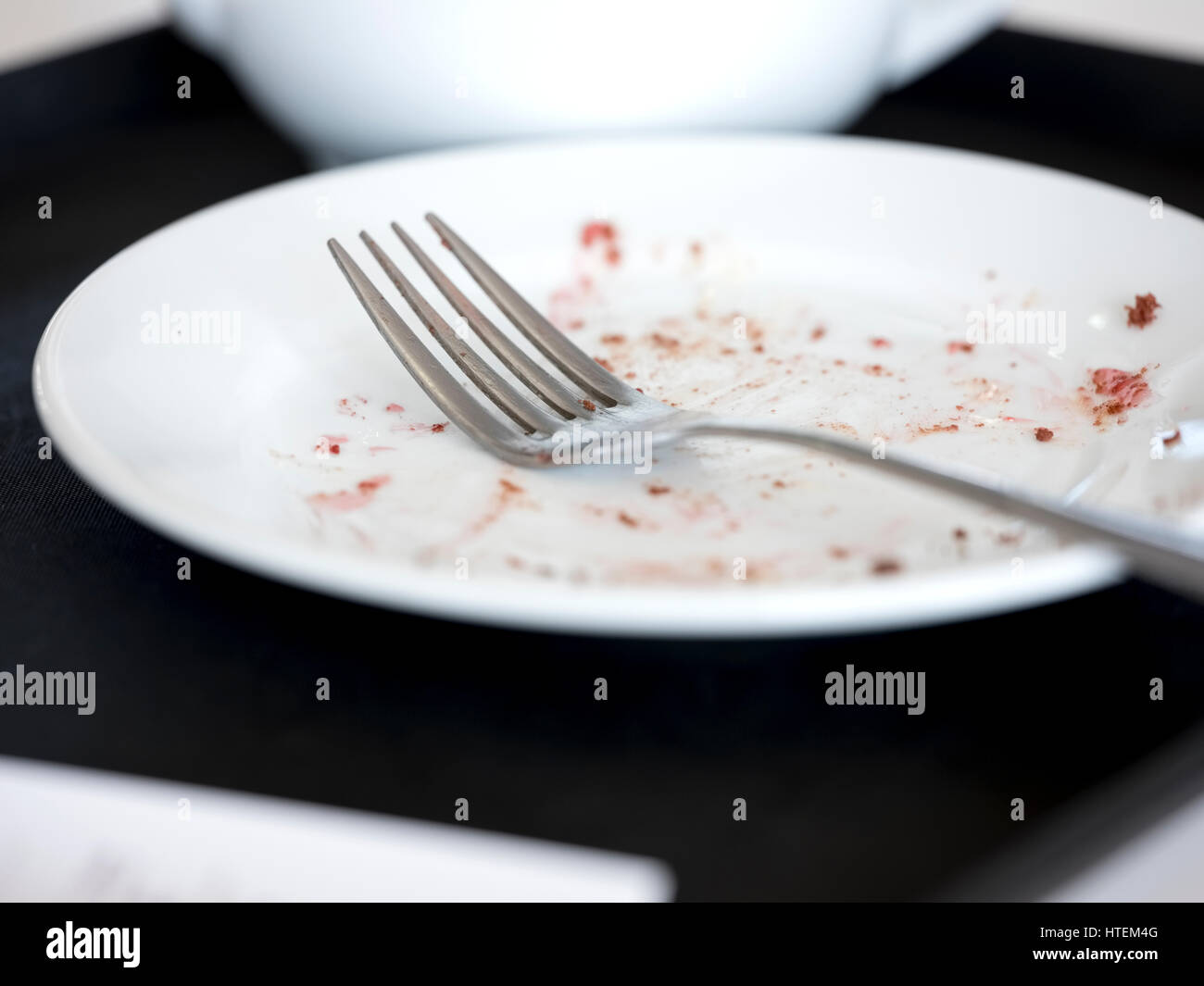 A used fork resting on an empty plate with crumbs left over beside a tea pot. Stock Photo