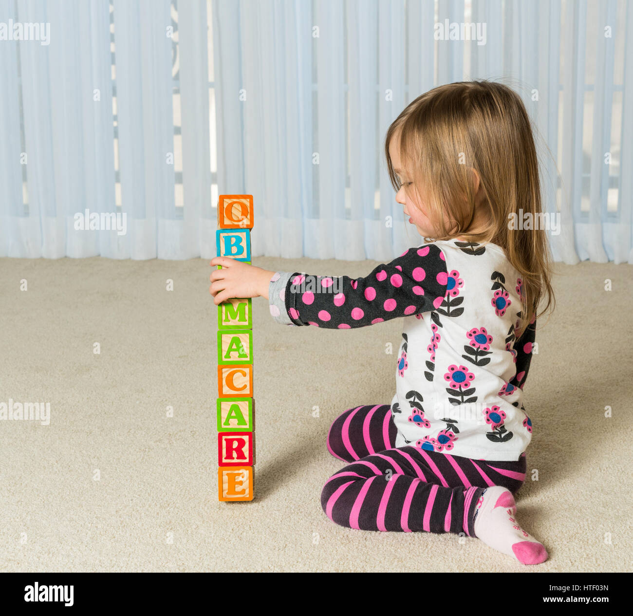 Young female toddler knocking down a tower of wooden blocks at home spelling Obamacare Stock Photo
