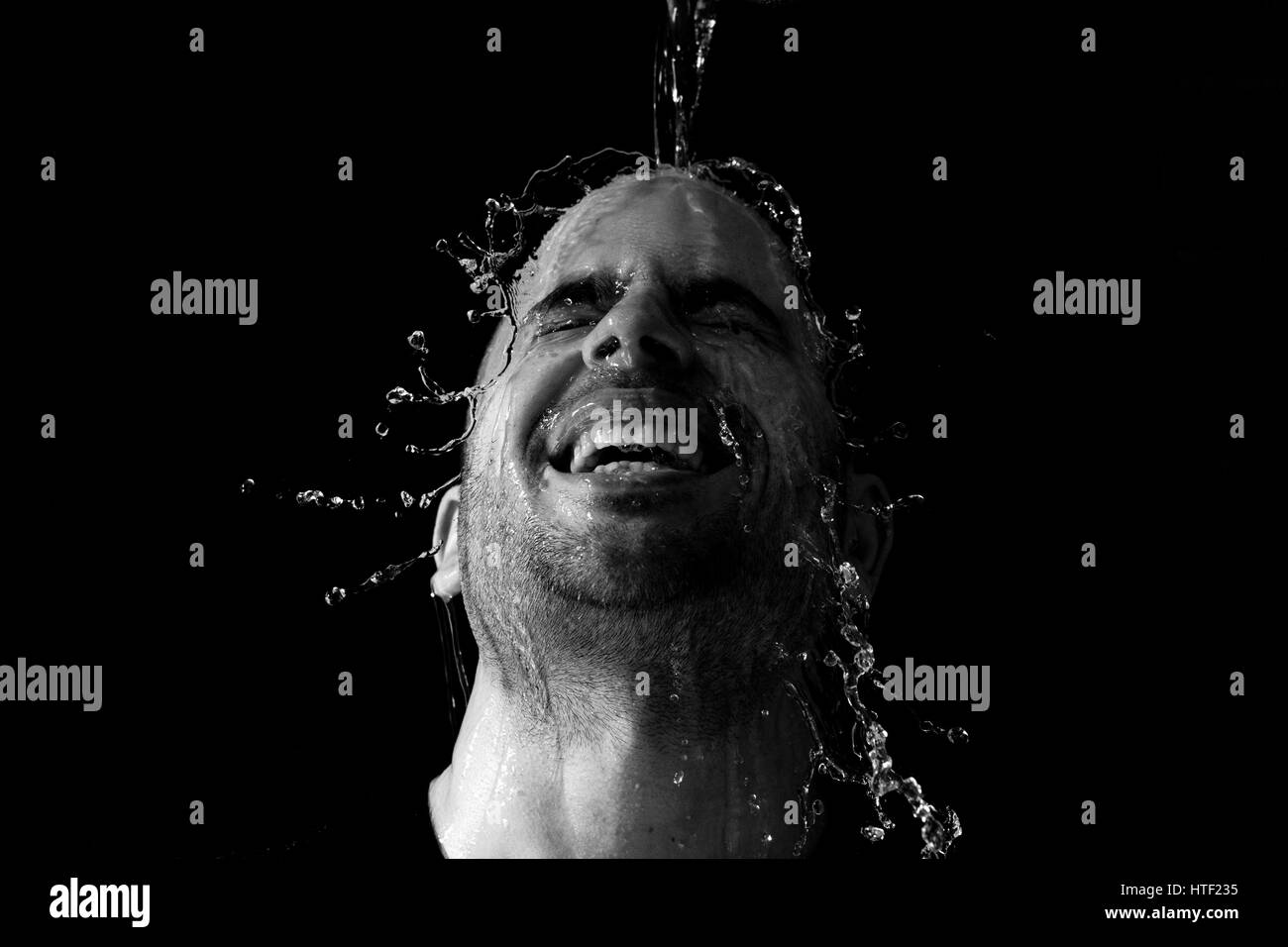 Portrait of a man being thrown water in the face against a black background Stock Photo