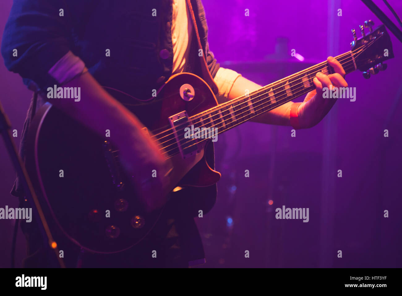 Electric guitar player on stage with purple scenic illumination, soft selective focus Stock Photo