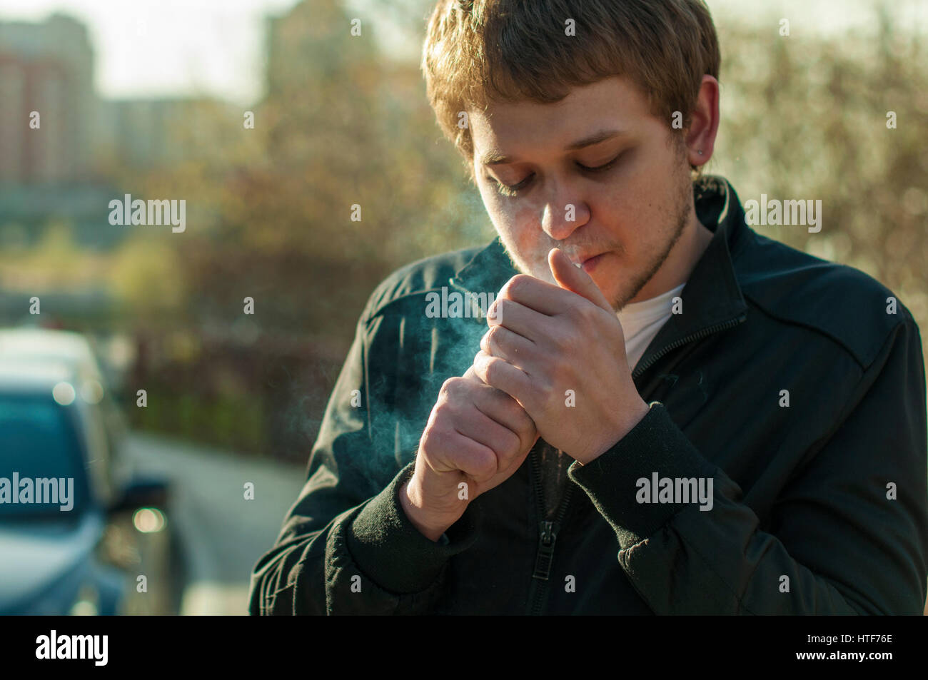 cigarette on ear A male hipster with a beard and earring in his ear, smoking a outdoors, a sunny afternoon Stock Photo Cigarette On A Boy Ear