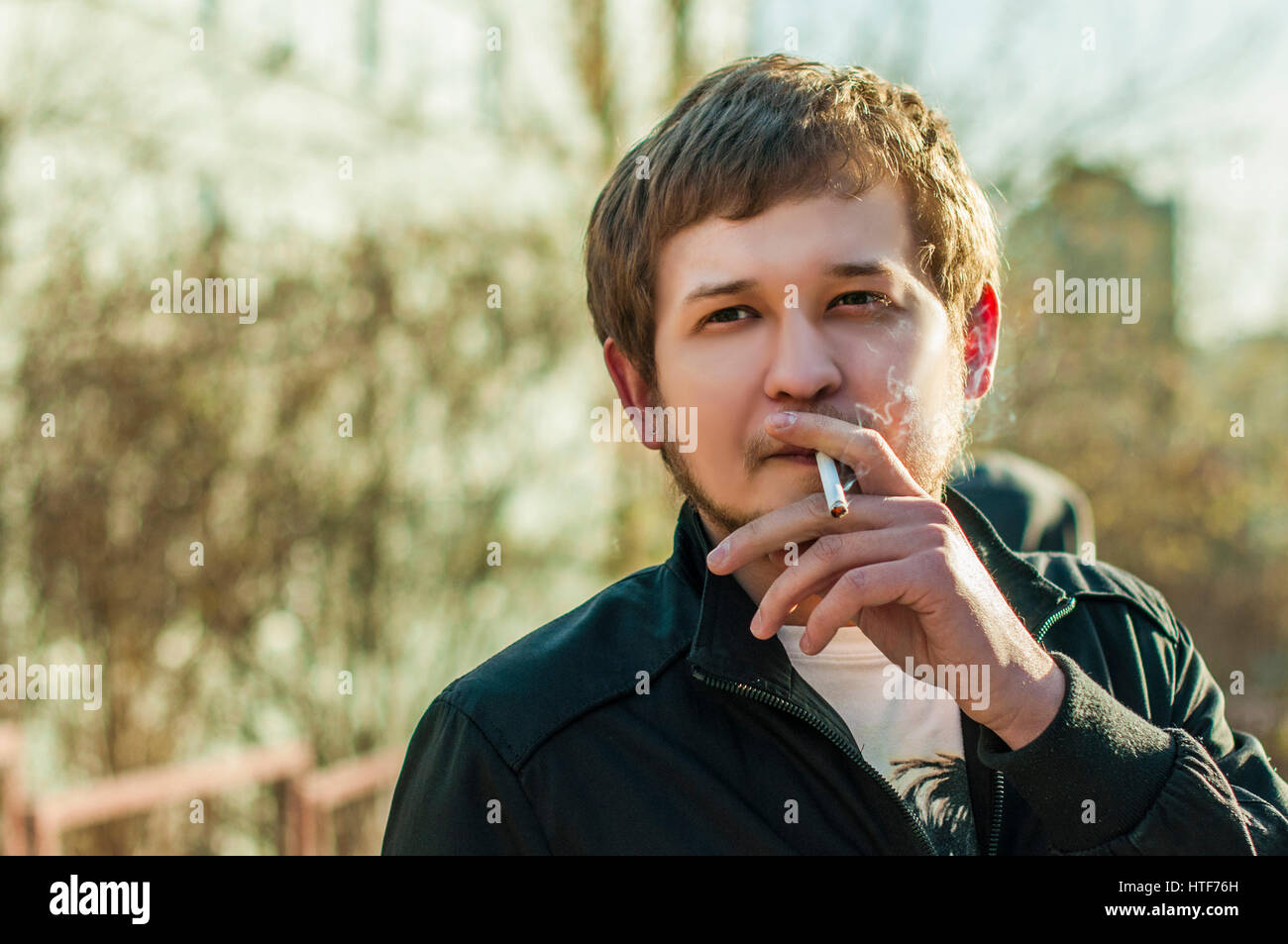 cigarette in ear A male hipster with a beard and earring in his ear, smoking a cigarette outdoors, a sunny afternoon Stock Photo cigarette in ear A male hipster with a beard and earring in his ear, smoking a cigarette outdoors, a sunny afternoon Stock Photo