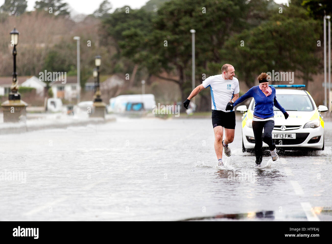 An undeterred male and female couple jogging through storm water puddles in Poole, Dorset as Storm Eleanor batters the south coast of England Stock Photo