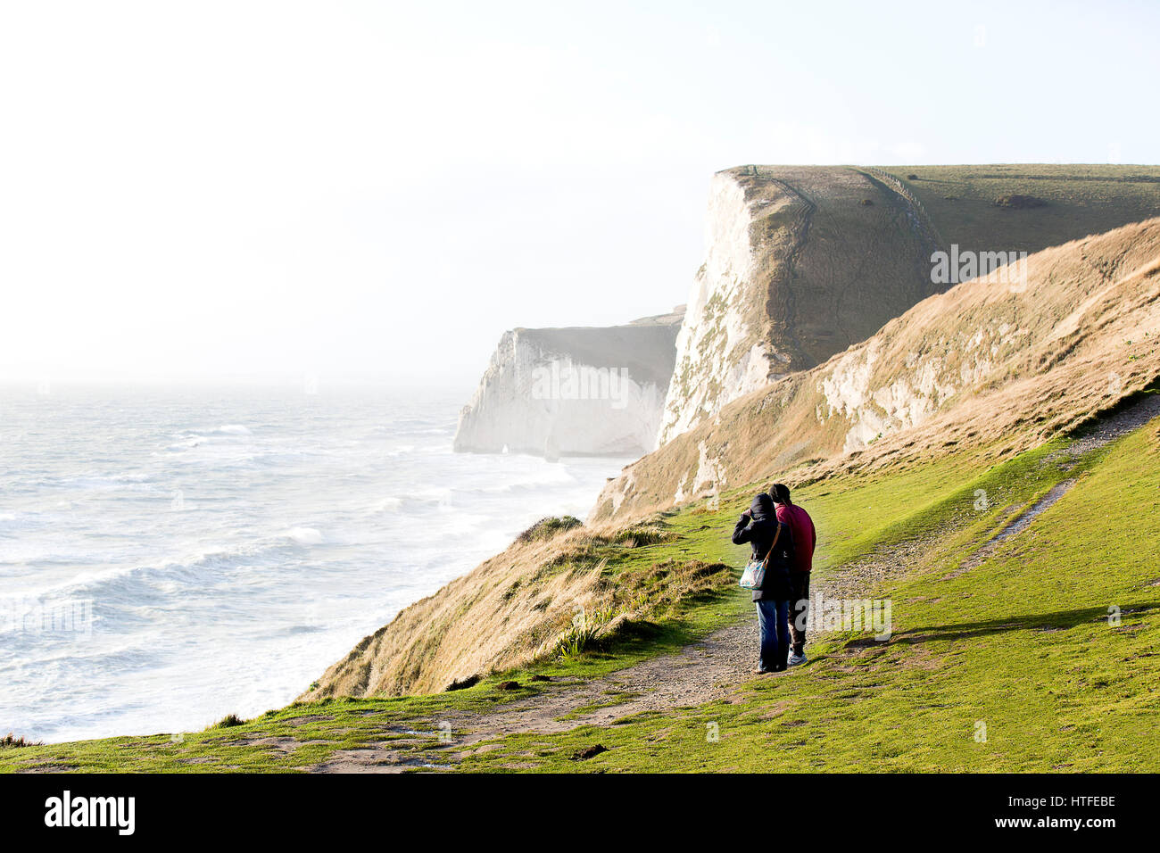 People standing on the Dorset Jurassic coast path at durdle door on a windswept afternoon. Man woman coastline stormy weather winter dor Stock Photo