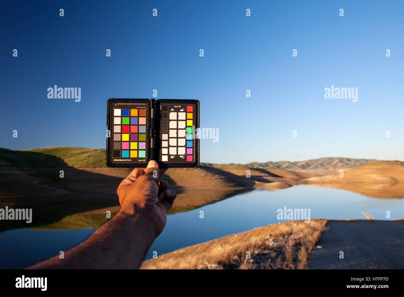 Hand holding out a color checker card with a landscape in the background. Stock Photo