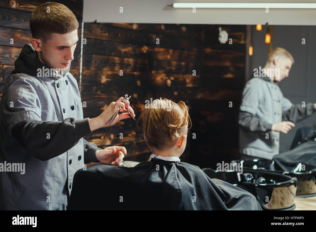 Little Boy Getting Haircut By Barber While Sitting In Chair At Barbershop. Barbershop Theme Stock Photo