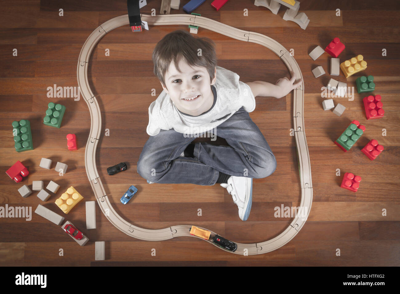 Happy child playing with toys train and railroad. Boy sitting on wooden ...