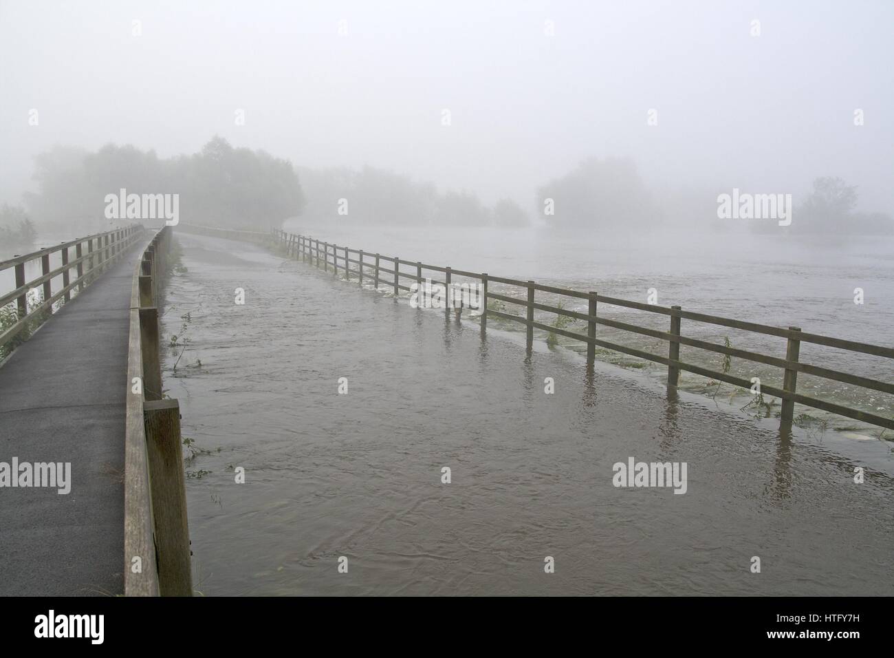 A view of a flooded river covering a road on a misty morning in Wiltshire, UK Stock Photo