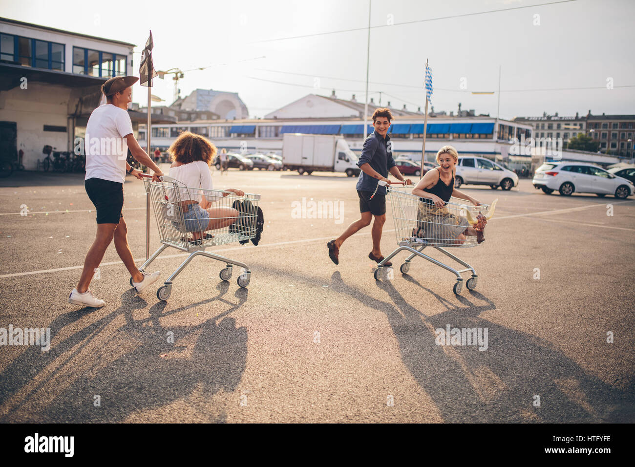 Young friends having fun on a shopping carts. Multiethnic young people playing with shopping cart. Stock Photo
