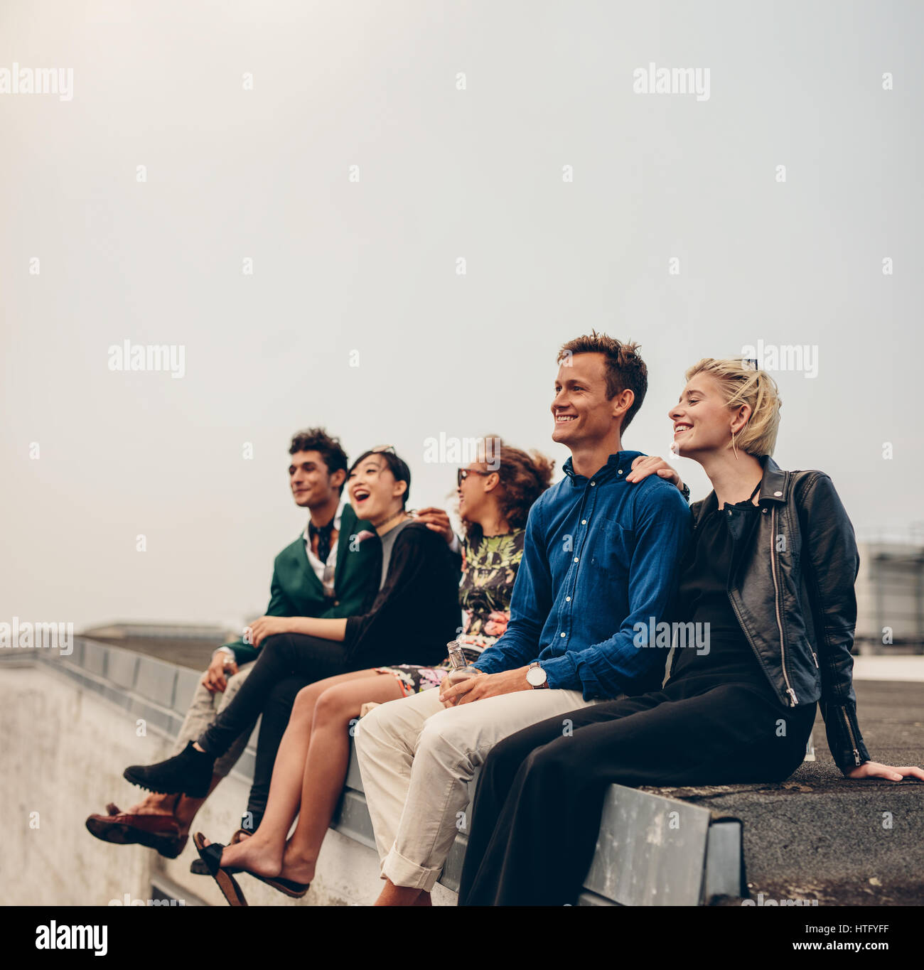 Happy young people relaxing on roof. Multiracial men and woman enjoying on terrace. Stock Photo