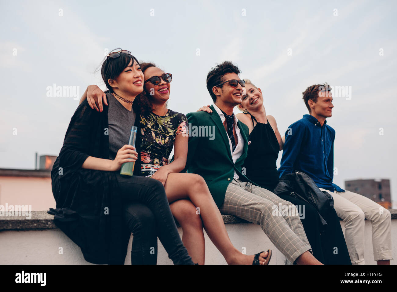 Shot of young friends hanging out together on rooftop. Multiracial group of people sitting on terrace and enjoying. Stock Photo