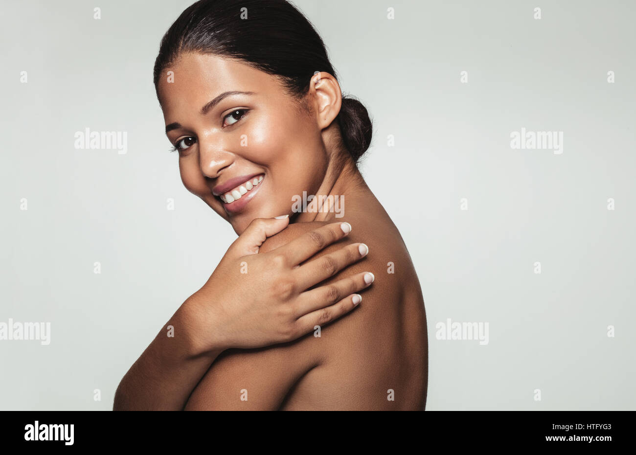 Portrait of pretty smiling woman covering her body with her hands and looking at camera against grey background. Close up of female model with beautif Stock Photo