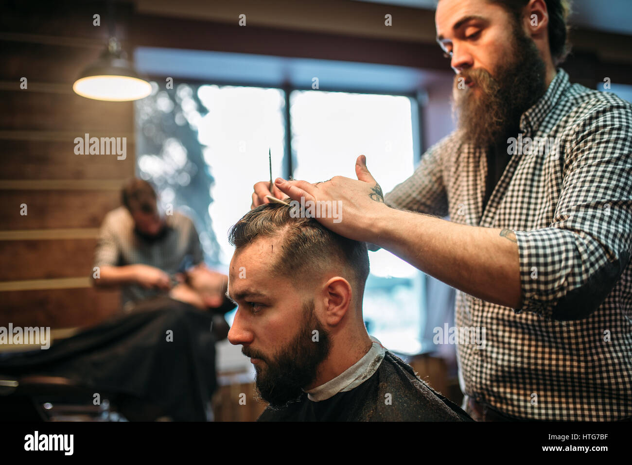Bearded hairdresser making male hipster hairstyle. Client man in black ...