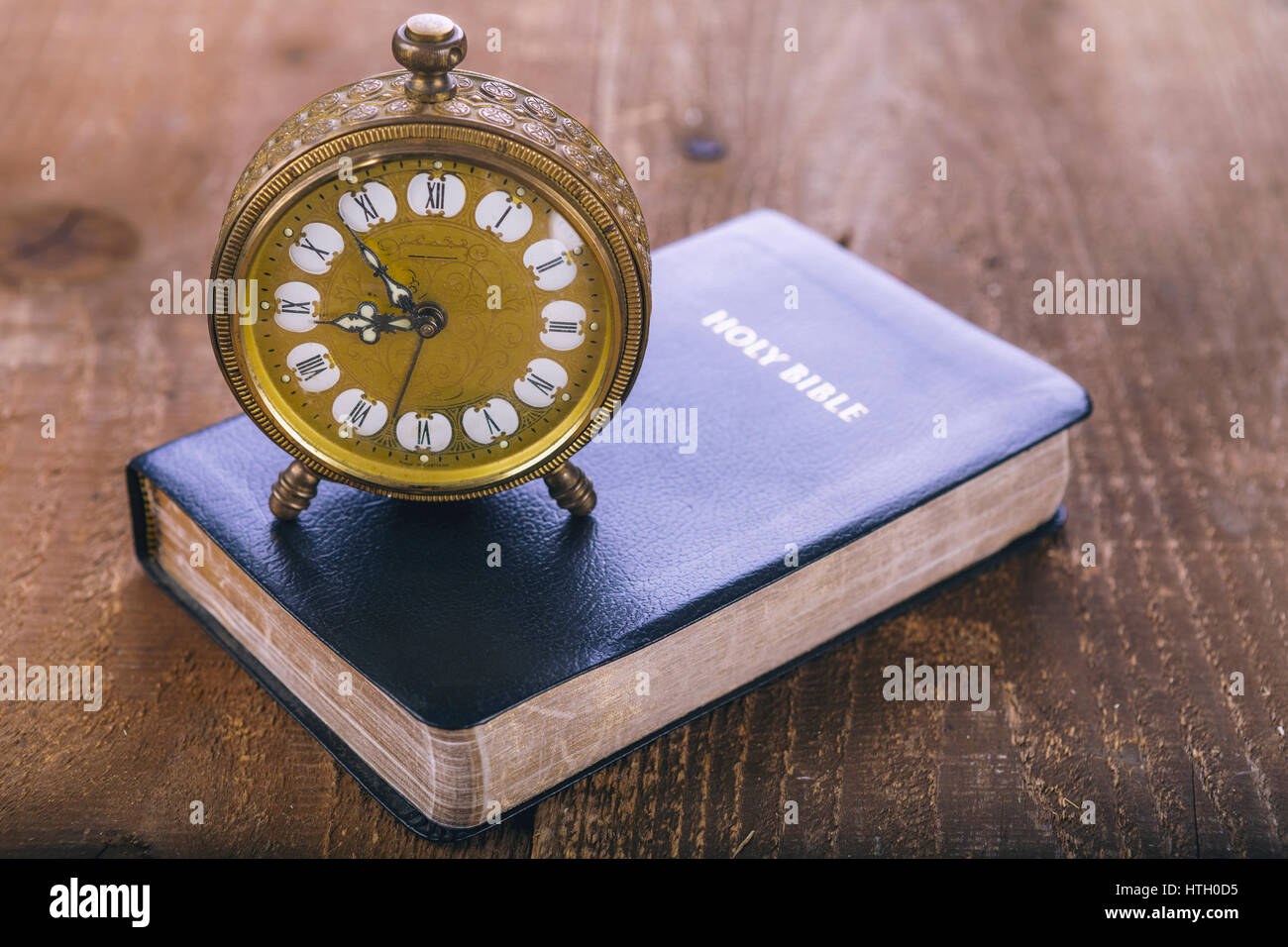Holy Bible and old gold alarm clock on wood table. Vintage colore. Stock Photo