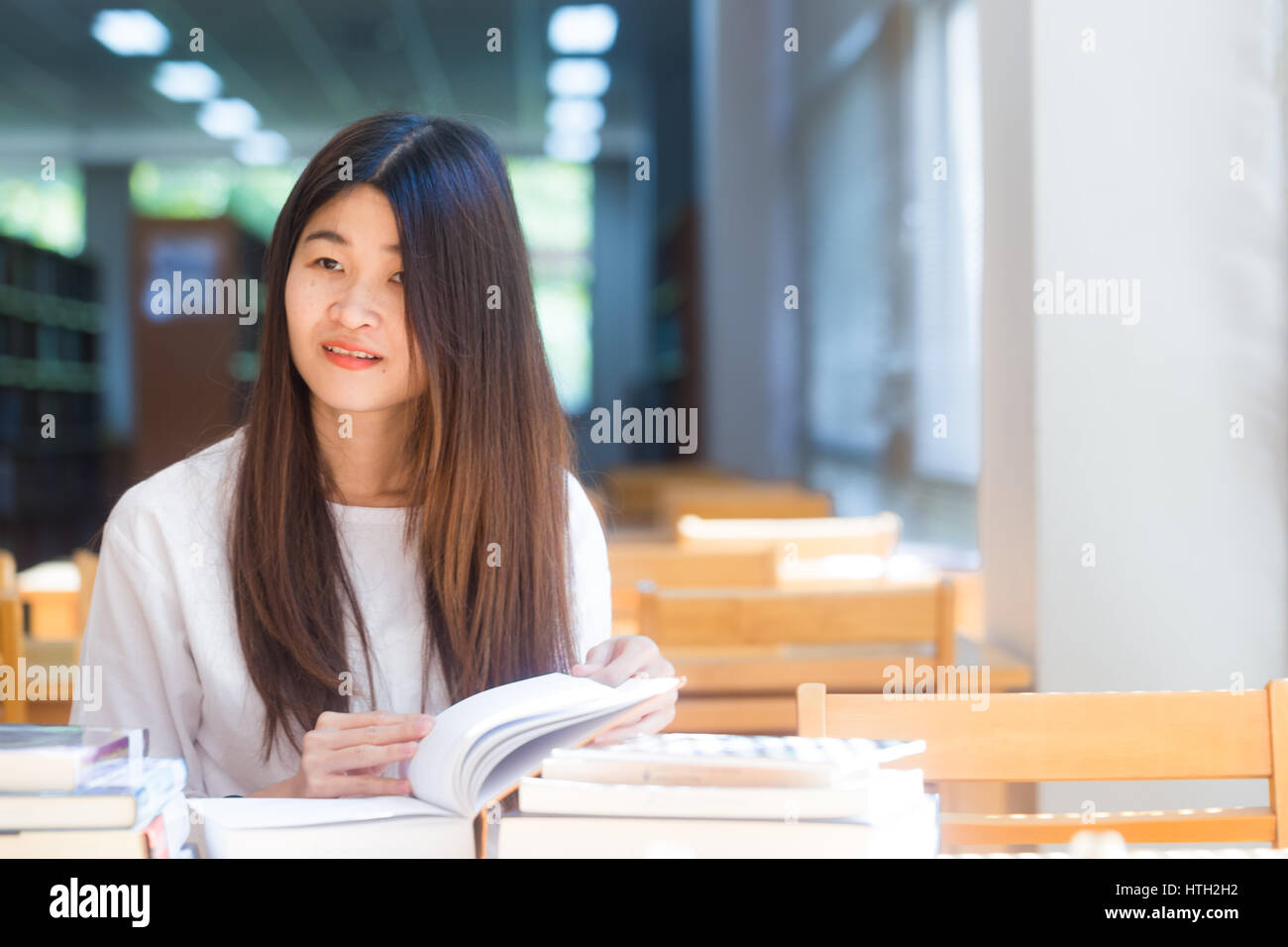 Happy asian student young woman thinking with book in library sitting ...