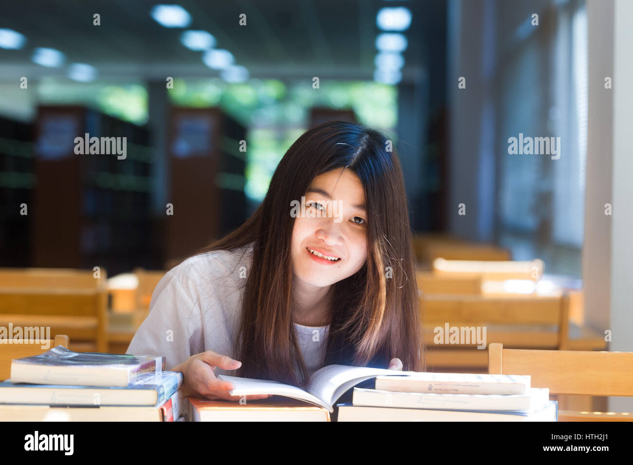 Happy asian student young woman thinking with book in library sitting ...