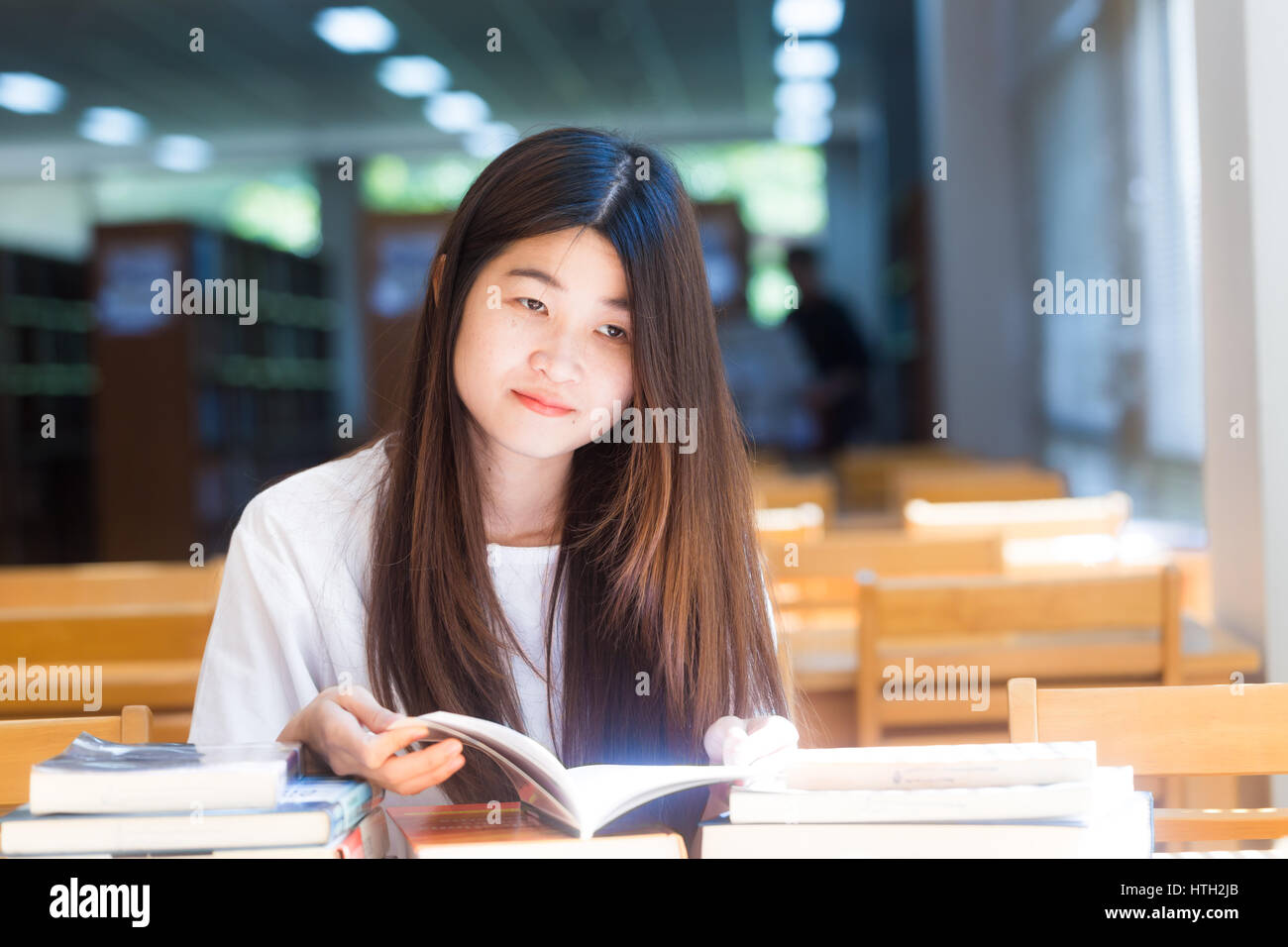 Happy asian student young woman thinking with book in library sitting ...