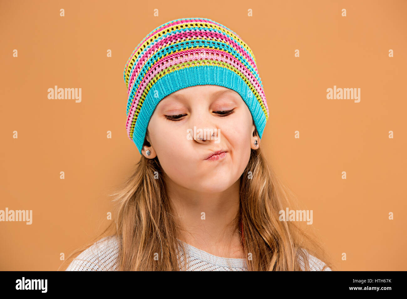 The face of unhappy sad teen girl in hat on brown studio background Stock Photo