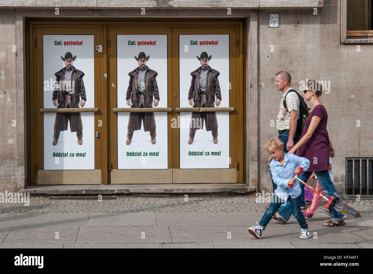 Strollers walking by 'Target: cash! Troops follow me!' Actor Chuck Norris in western attire, in bank advertising poster in Wroclaw, Poland Stock Photo