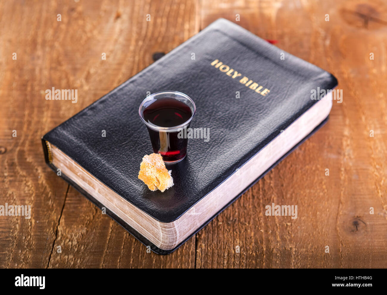 Taking Communion. Cup of glass with red wine, bread and Holy Bible on wooden table close-up. Focus on glass Stock Photo