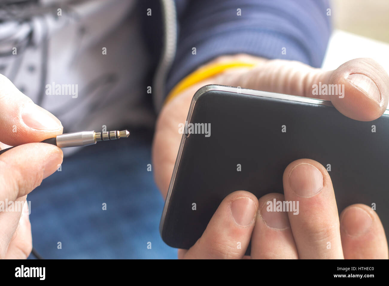 Close up view of Hand holding black mobile phone with earphone cable (plug, connection) stereo jack music port. Stock Photo