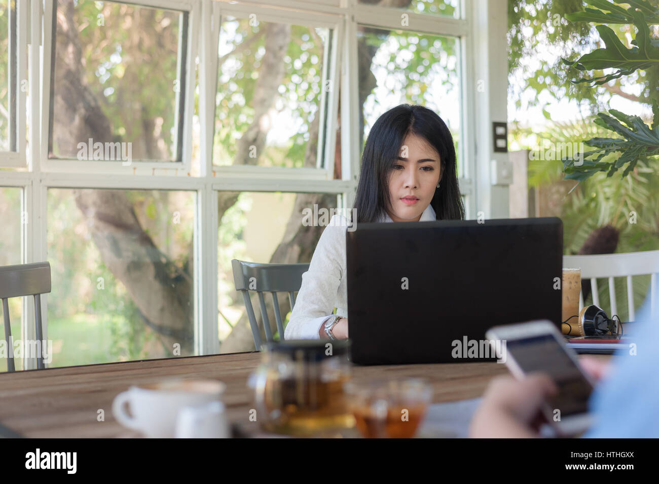 Young Asian businesswoman working online while being concentrate on her laptop computer while sitting in coffee shop. Self-employed and freelance work Stock Photo