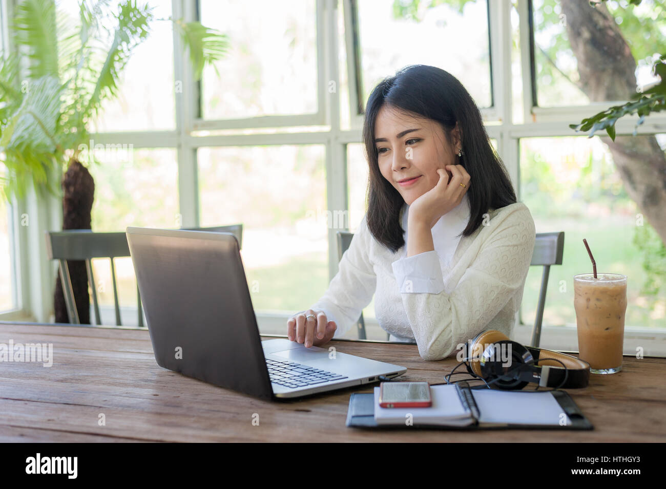 Young Asian businesswoman working online with laptop computer while sitting in coffee shop. Self-employed and freelance worker business activity conce Stock Photo
