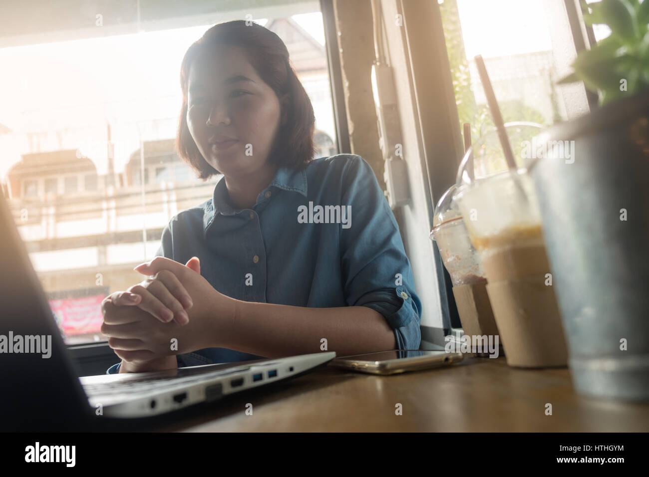 Young Asian woman looking at her laptop computer while working in coffee shop. Freelance worker with online business activity concept. Hipster in digi Stock Photo