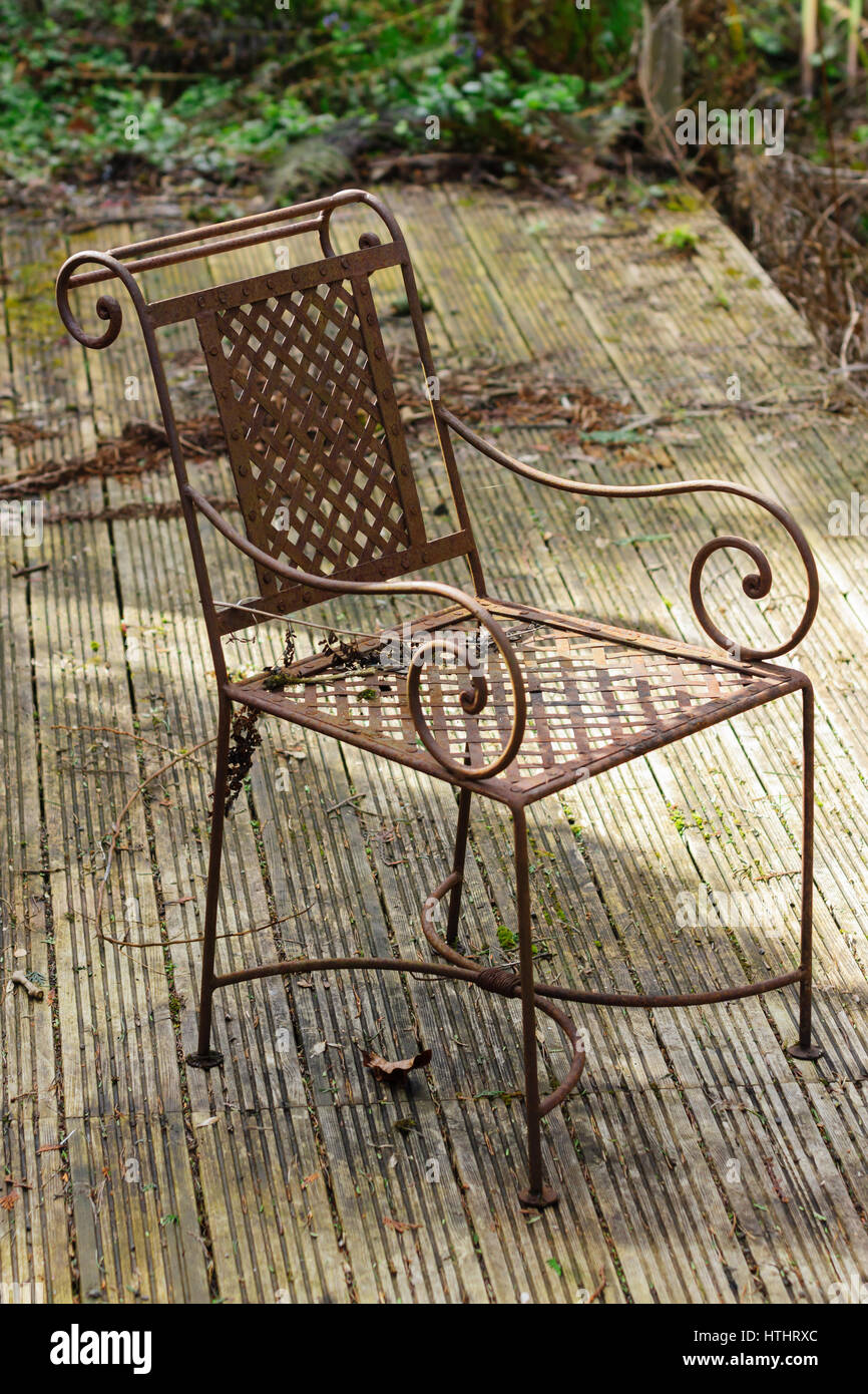Rusty abandoned garden chair on neglected wooden decking in an overgrown poorly maintained garden Stock Photo