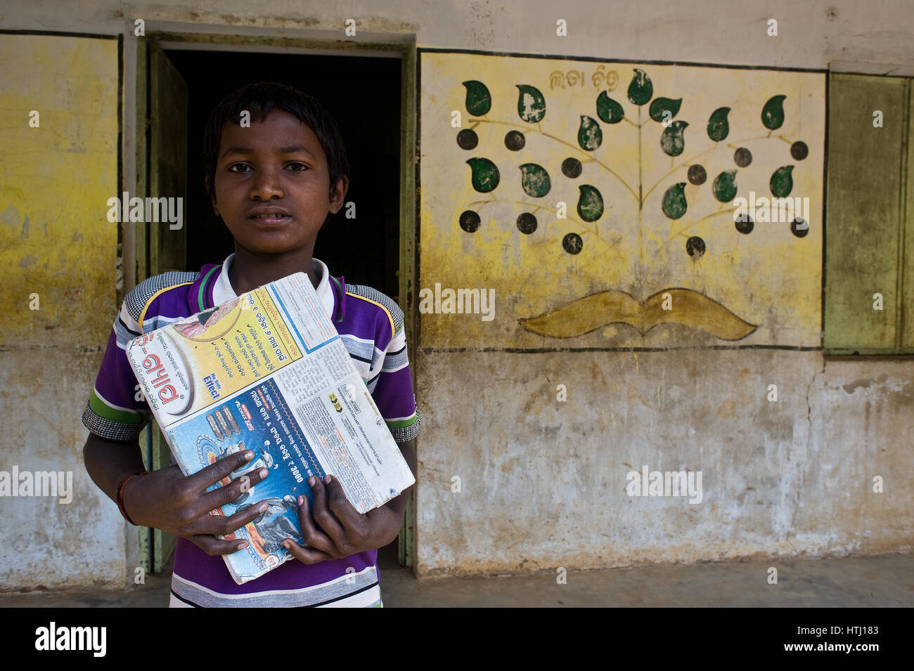 A boy belonging to the Dongria Khond tribe is holding his textbook in front of a classroom ( India) Stock Photo