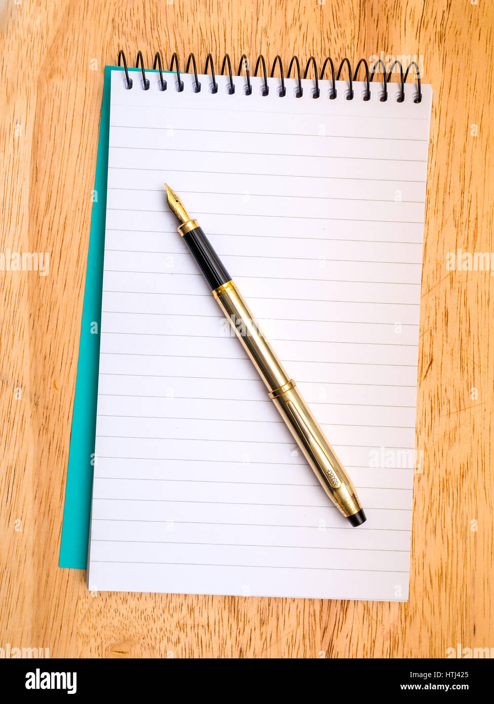 A Cross brand gold fountain pen resting on a spiral bound reporters notebook Stock Photo
