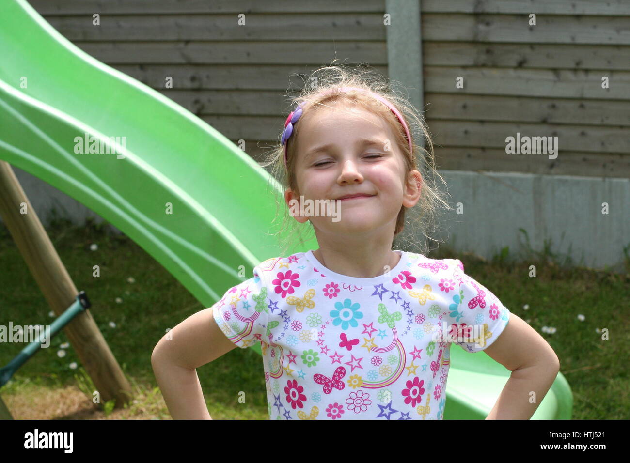 Little blonde girl child kid having fun, playing and messing, making a funny face, funny gesture, childhood joy, funny concept, joke, hand on hips Stock Photo