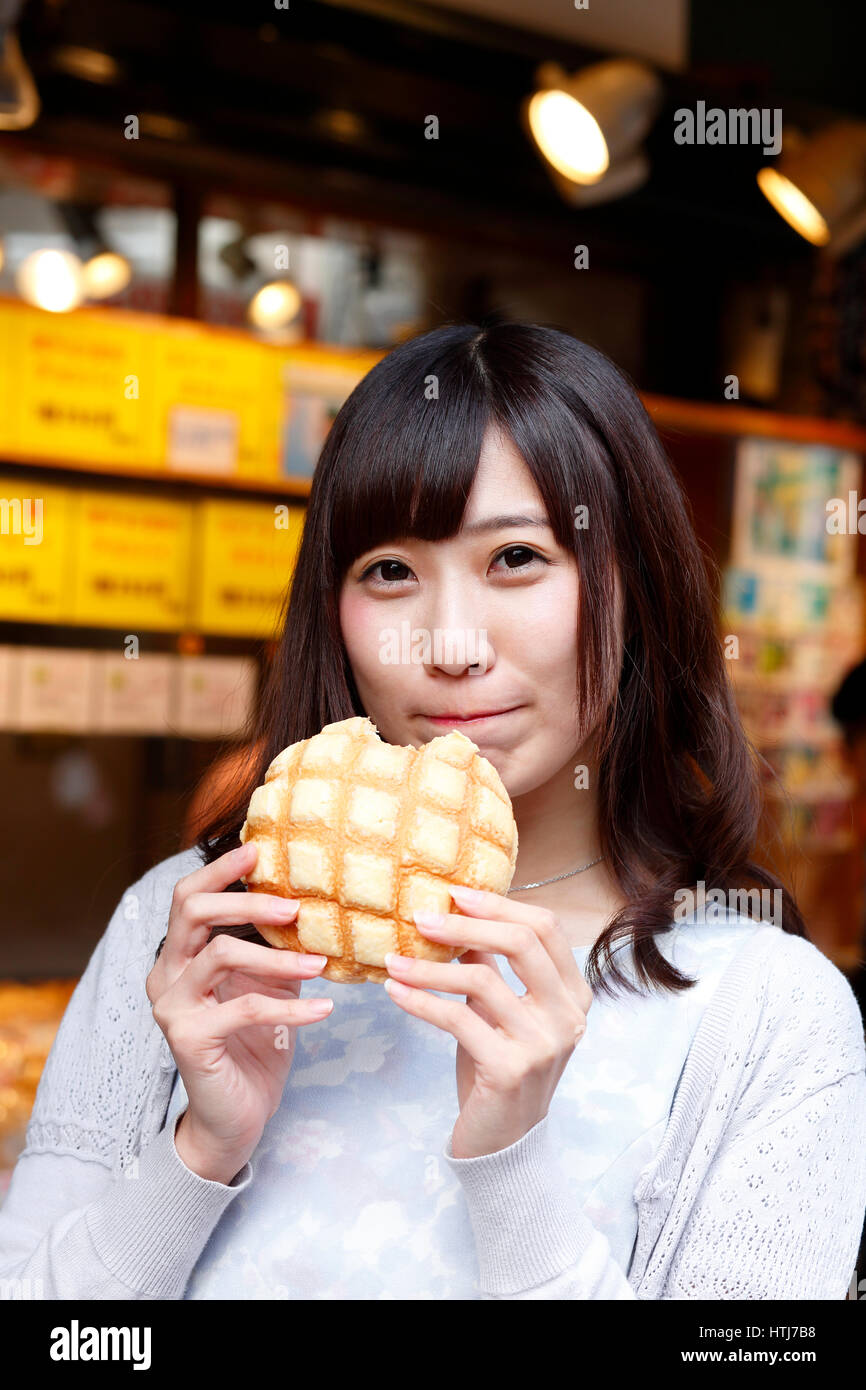 Fashionable Japanese woman eating bread at a traditional shopping street, Tokyo, Japan Stock Photo
