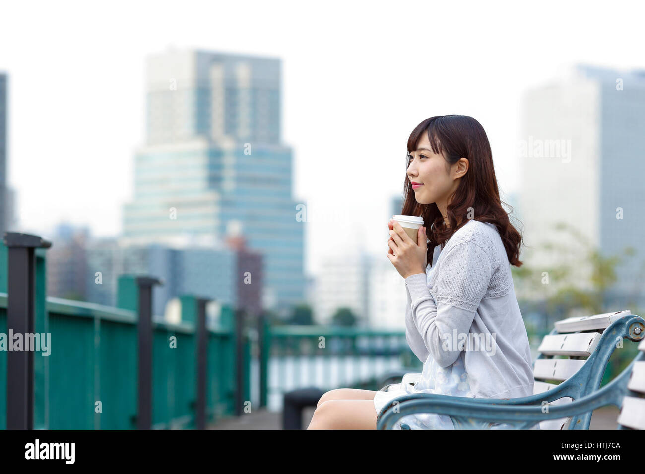 Fashionable Japanese woman with coffee sitting on a bench by the river, Tokyo, Japan Stock Photo