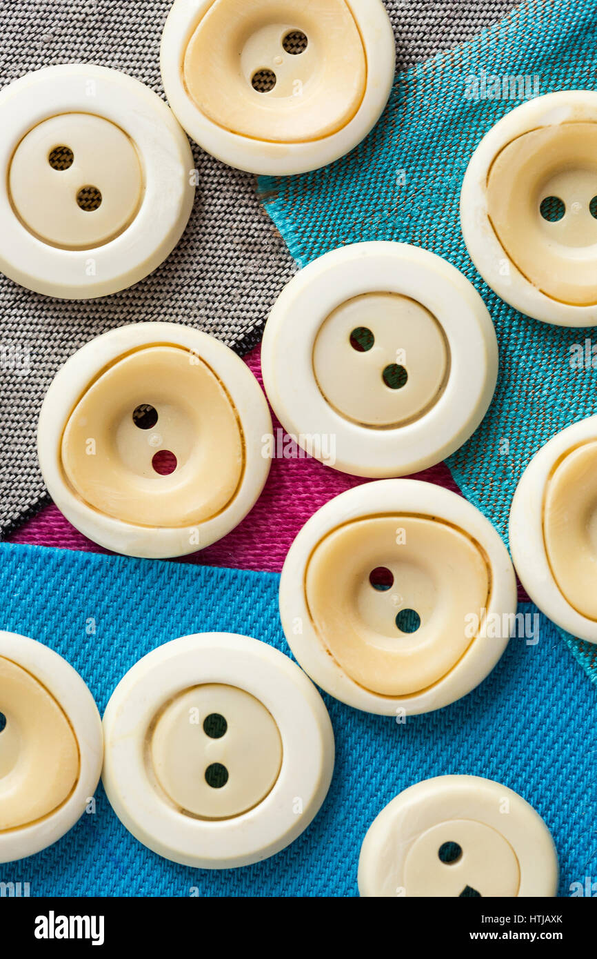 concept with beige monophonic buttons on pieces of colored fabric, macro, top view. Stock Photo