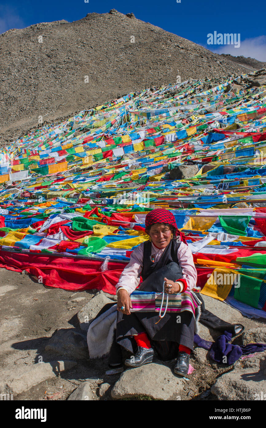 Tibetan nomad woman pilgrim sitting on rock, holding prayer beads in hand at Dolma La top en route Mt. Kailash Kora Stock Photo